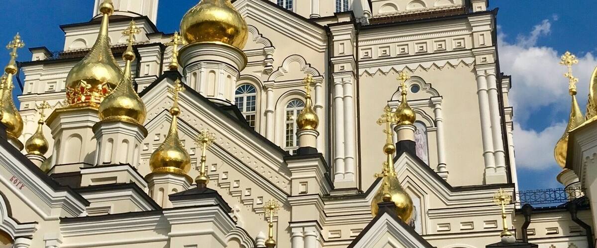 A white church with golden domes and crosses under a blue sky.