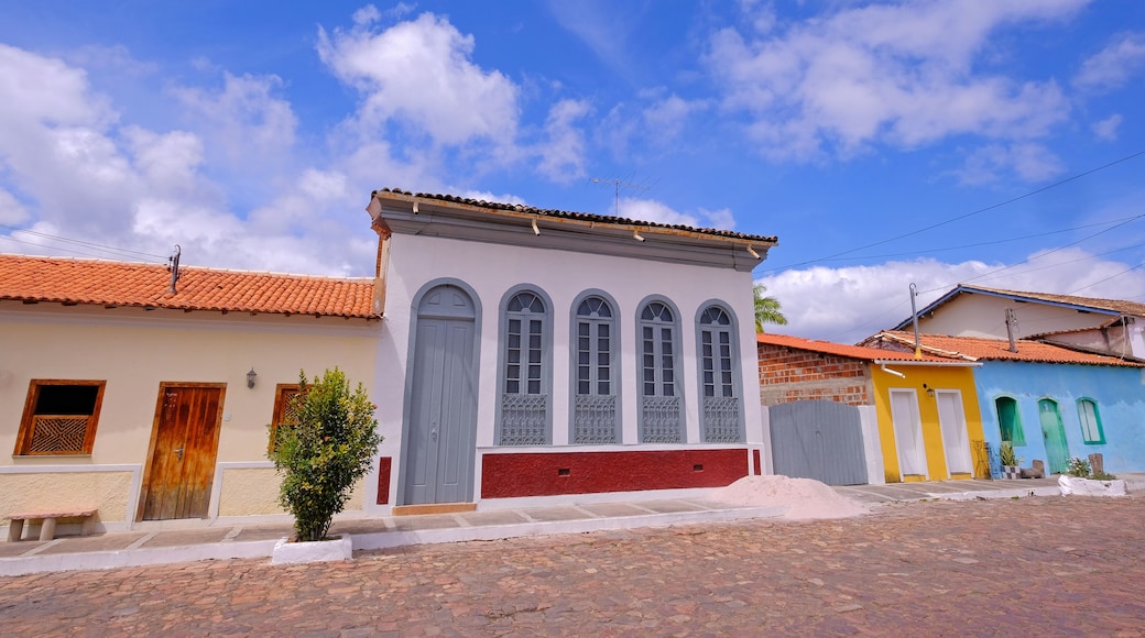 A street with colorful buildings, a cobblestone road, and a clear blue sky with clouds.