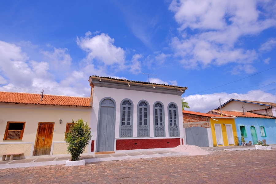 A street with colorful buildings, a cobblestone road, and a clear blue sky with clouds.