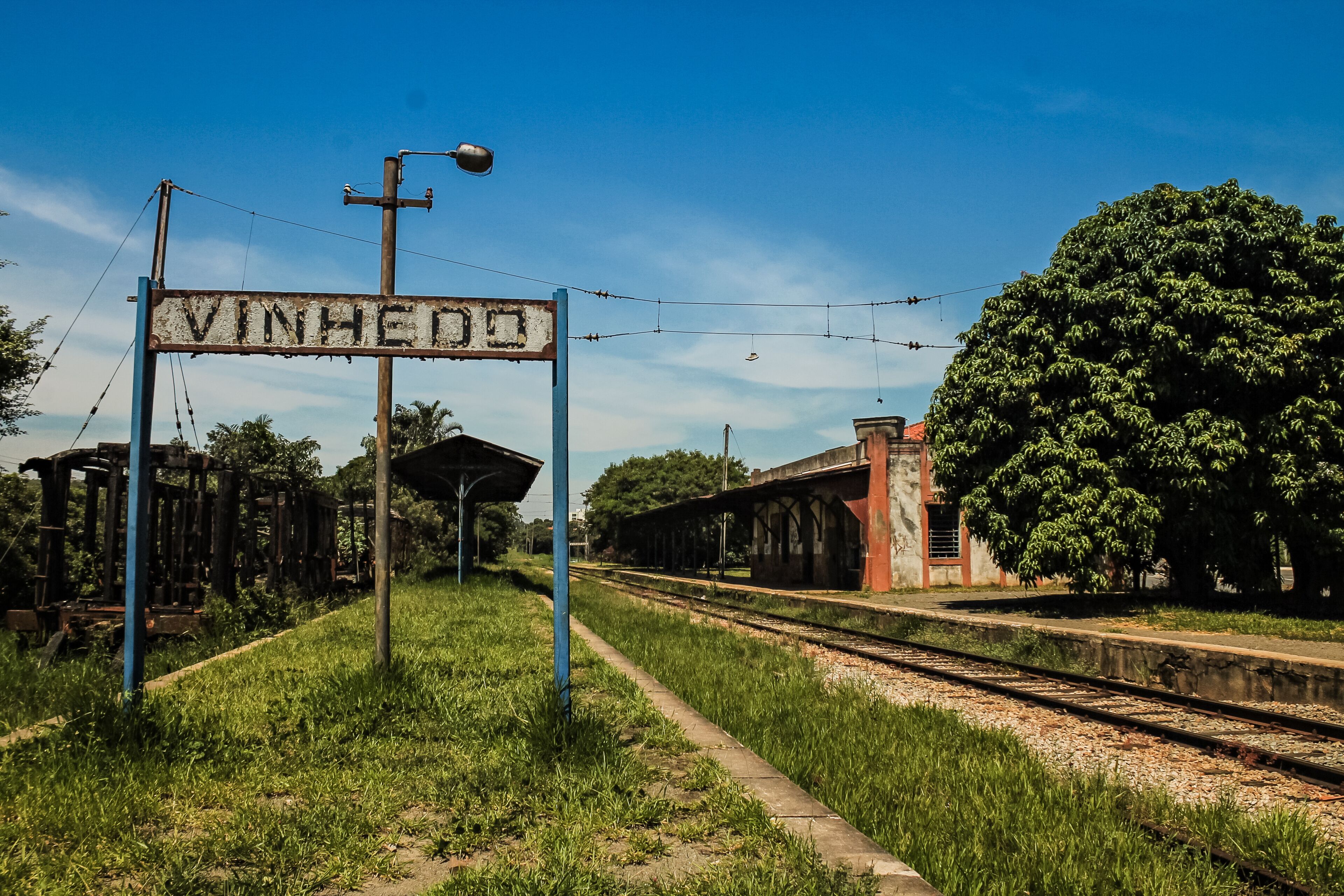 A railway station with a sign reading 'VINHEDO,' surrounded by greenery and a clear blue sky.