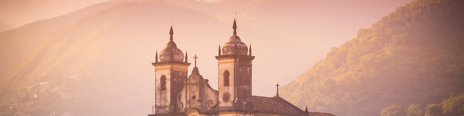 Una iglesia con dos campanarios, rodeada de abundante vegetación y colinas.