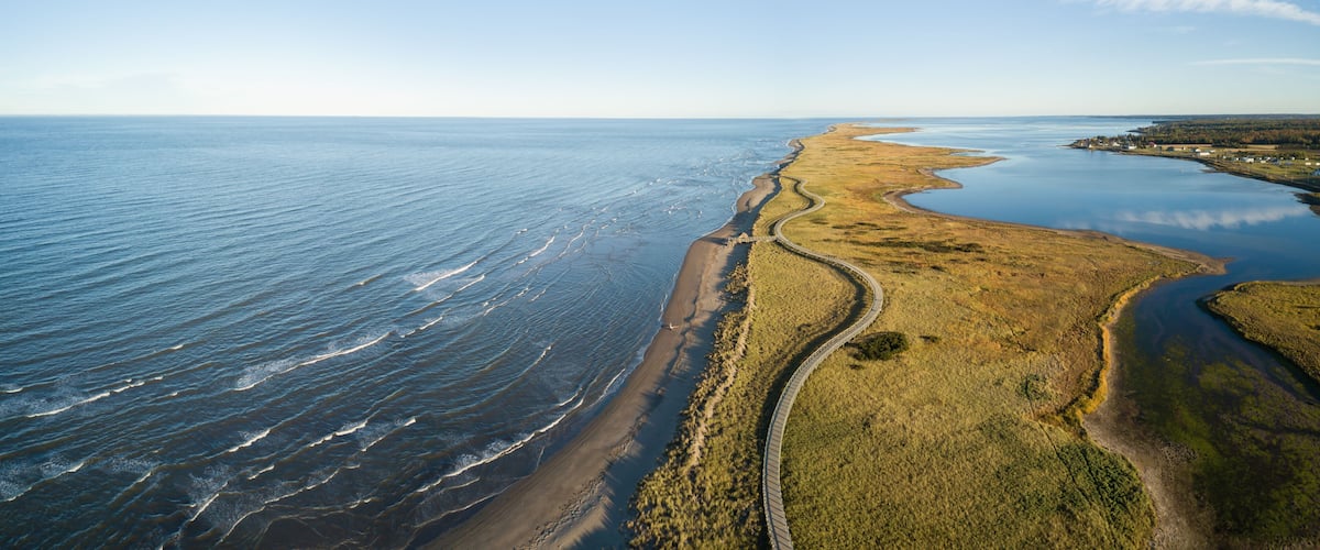 A coastal landscape with a sandy beach, a winding road, and a calm sea.