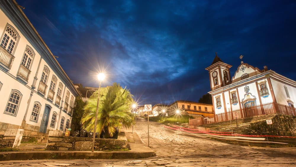 A cobblestone street at night with historic buildings, a palm tree, and a church with a bell tower.
