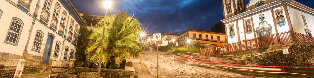 A cobblestone street at night with historic buildings, a palm tree, and a church with a bell tower.