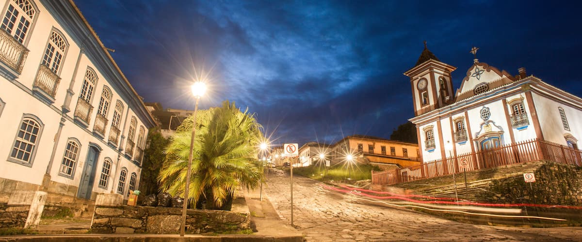 A cobblestone street at night with historic buildings, a palm tree, and a church with a bell tower.