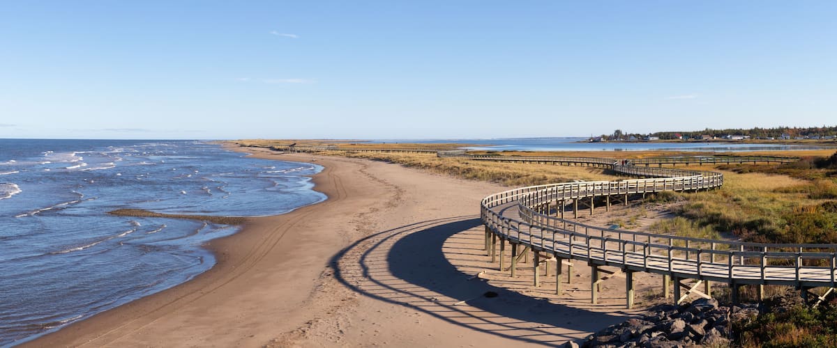 A sandy beach with a wooden boardwalk curving along the shore.