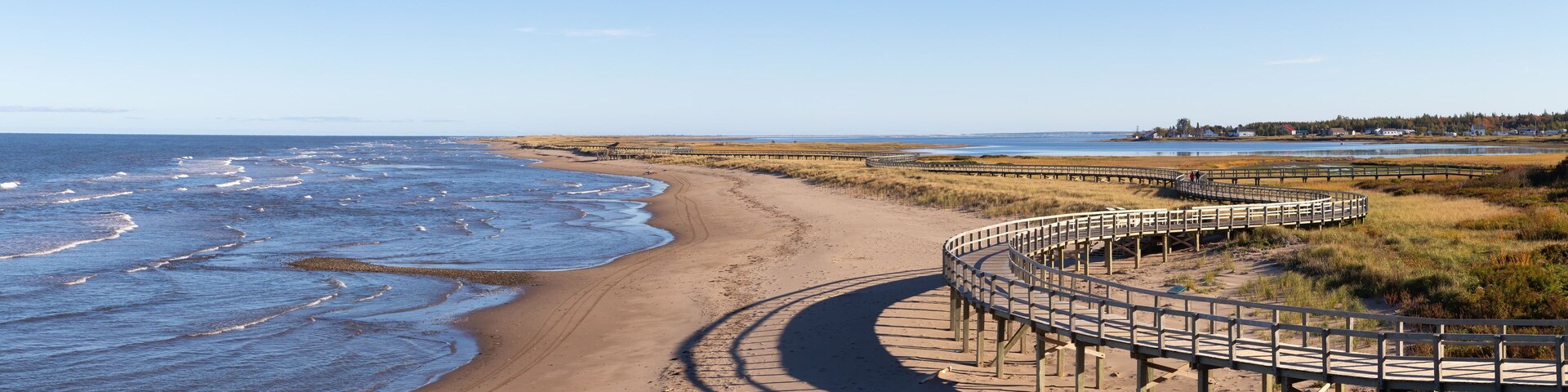 A sandy beach with a wooden boardwalk curving along the shore.