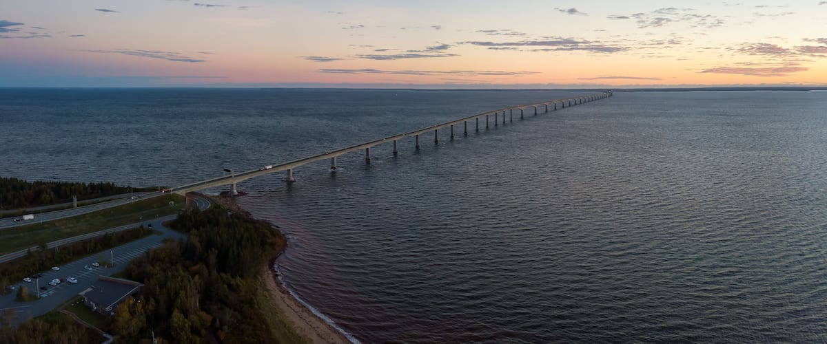 A coastal road with a long bridge extending into the sea, surrounded by trees and a clear sky.