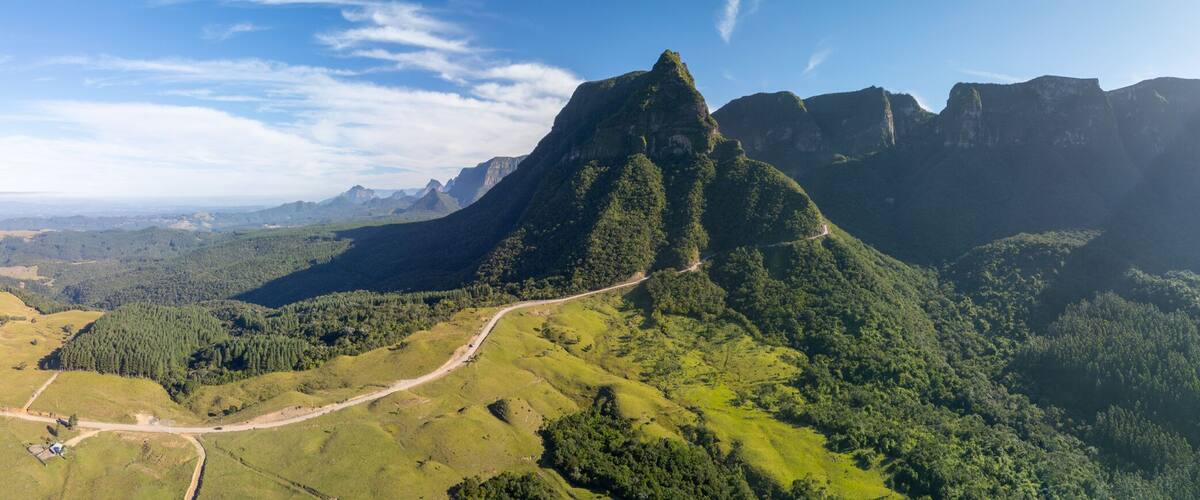 A mountain range with a prominent peak, surrounded by dense forests and a winding road.