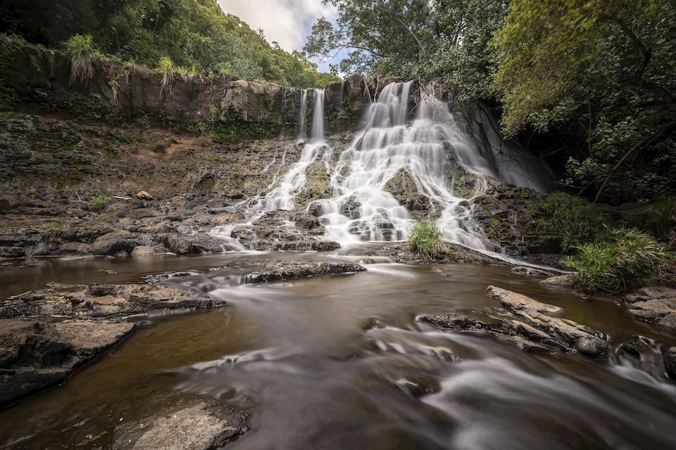 A waterfall cascading over rocks into a river surrounded by lush greenery.