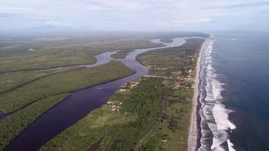 Un paysage côtier avec une rivière se jetant dans l’océan, entouré d’une végétation luxuriante et d’une plage où les vagues déferlent sur le rivage.