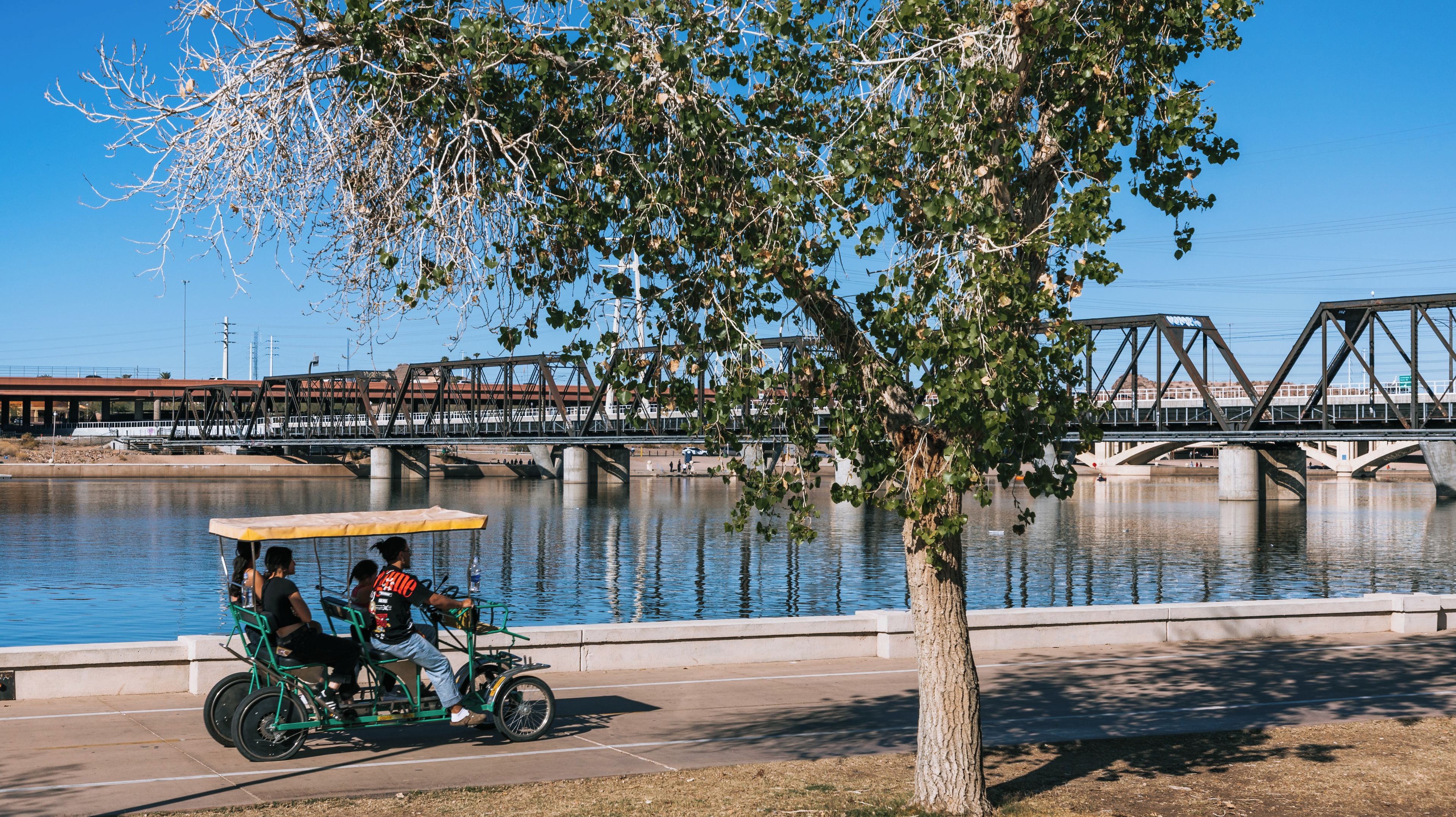 Um rio com uma ponte, uma árvore e uma bicicleta verde com passageiros.