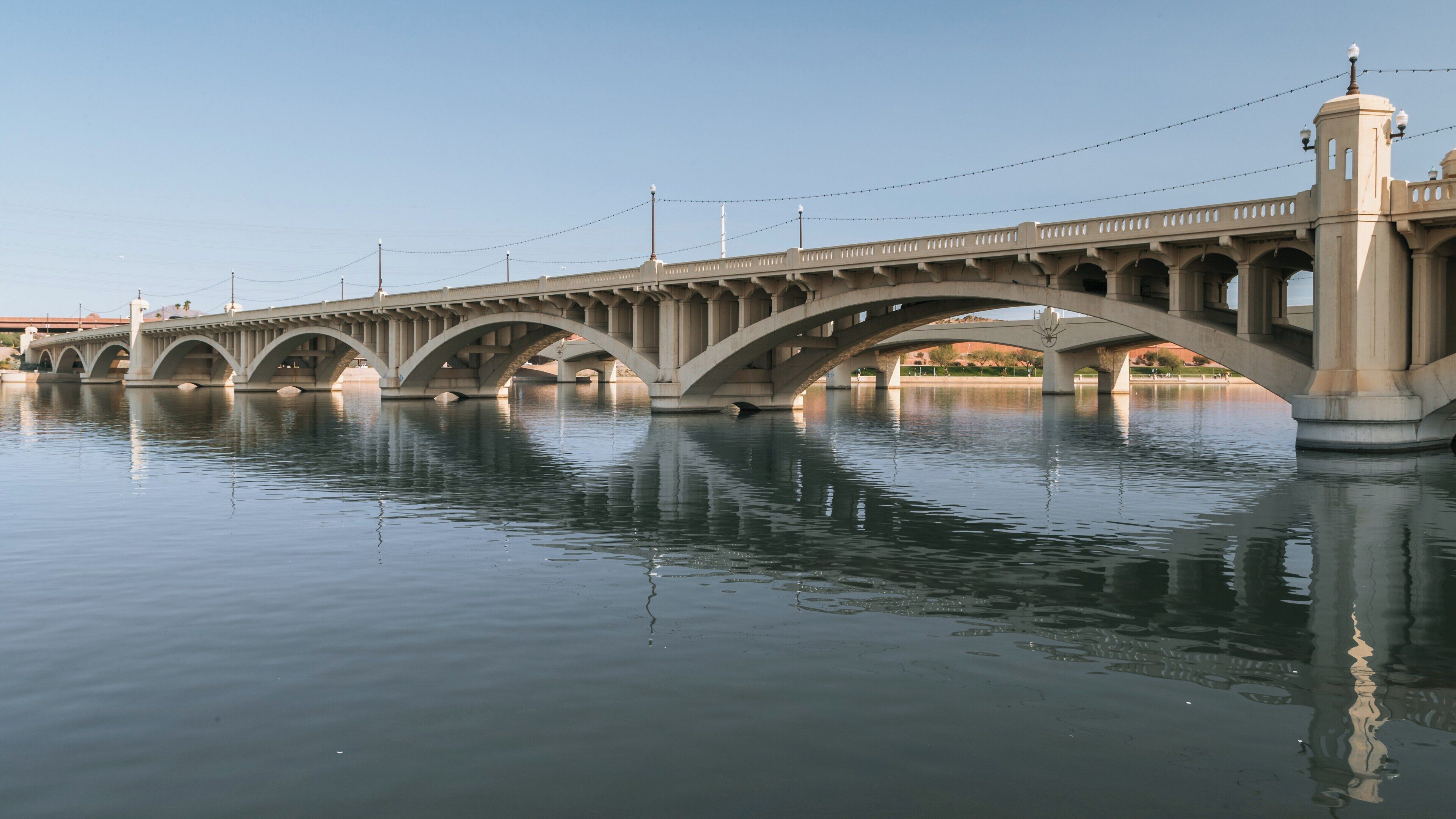 Tempe Beach Park offers a serene view of the iconic Tempe Town Lake Bridge reflecting in the water under a clear sky in Arizona