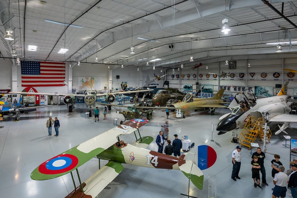 A museum with various military aircraft on display, including a green and white biplane with a red and blue target on its wing.