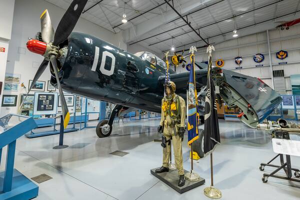 Uma aeronave militar antiga com o número 10 na lateral, um manequim de piloto e diversos símbolos militares nas paredes.