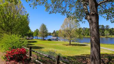 A gorgeous summer landscape in the garden with a lake and lush green trees, grass and plants, a brown wooden boathouse, red flowers, and wooden fence with blue sky at Callaway Gardens in Pine Mountain