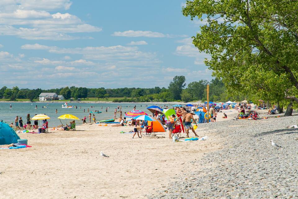 Una spiaggia affollata con persone, ombrelloni e un lago sullo sfondo.