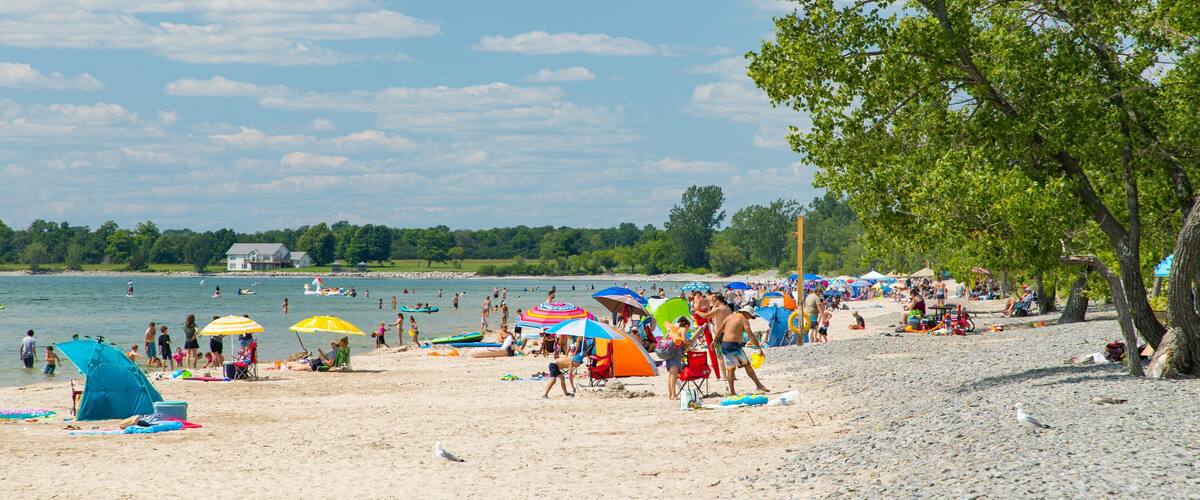 A crowded beach with people, umbrellas, and a lake in the background.