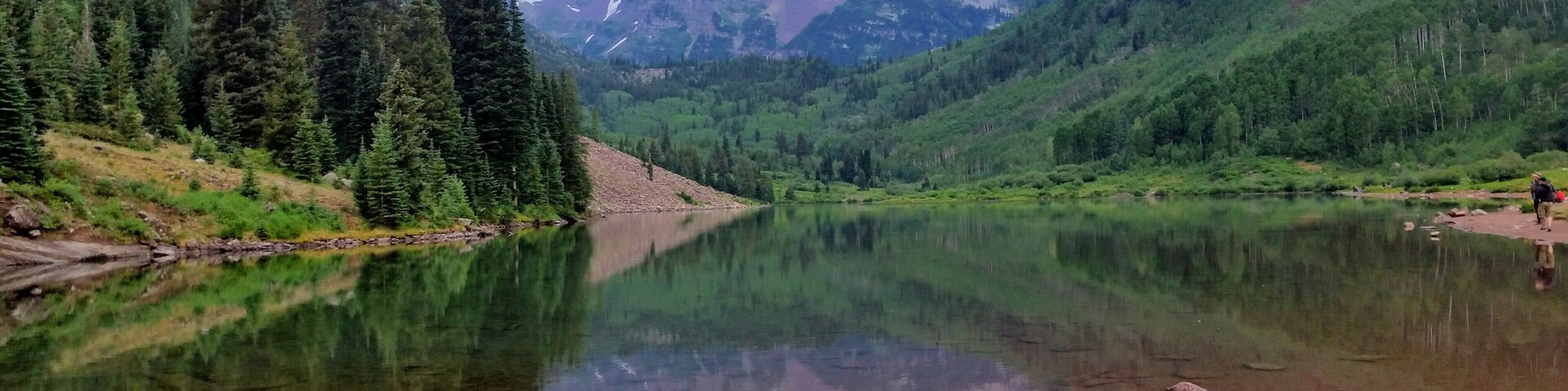 Un lago tranquilo rodeado de bosques densos y montañas elevadas.