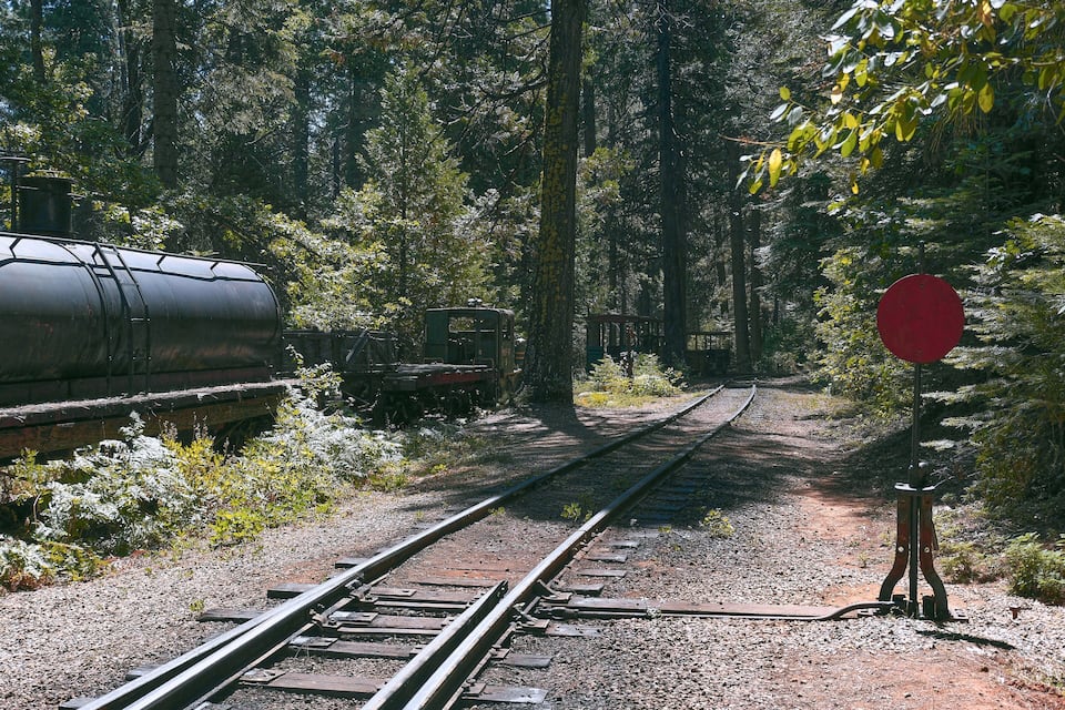 A railway track with a red stop sign and a train in a forested area.