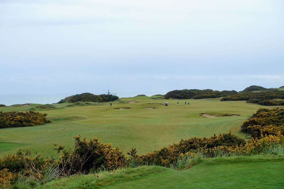 A golf course with rolling hills and a distant view of the sea.