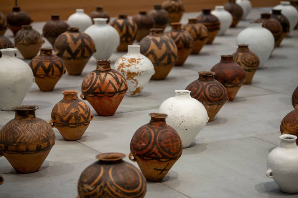 A collection of variously shaped and decorated pottery vases arranged on a tiled floor.