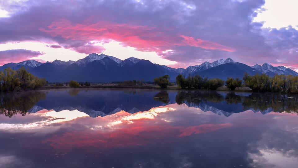 A mountain range reflected in a calm lake with a colorful sky.