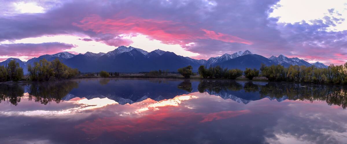 A mountain range reflected in a calm lake with a colorful sky.