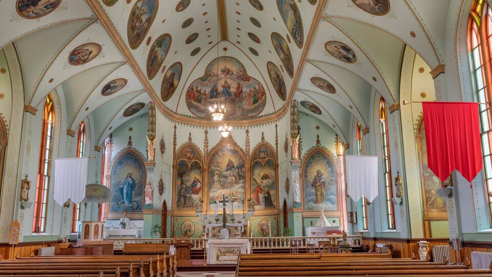 An ornate church interior with wooden pews, a central altar, and elaborate ceiling frescoes.