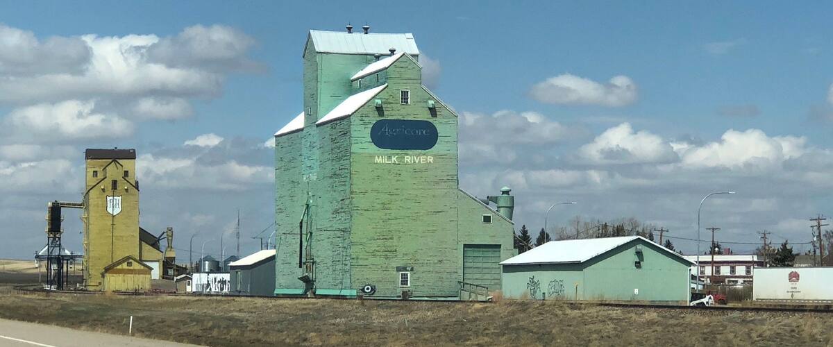 A large green silo with 'Agricore Milk River' written on it, a yellow silo, and a small building with a 'FH' logo.