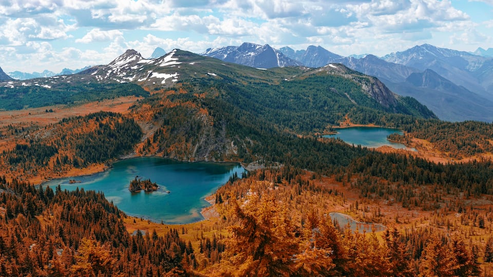 A mountainous landscape with two turquoise lakes surrounded by dense forests and snow-capped peaks.