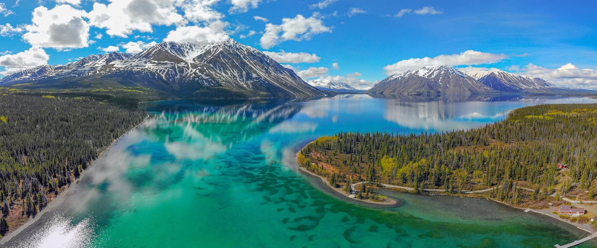 A turquoise lake surrounded by dense forests and snow-capped mountains.