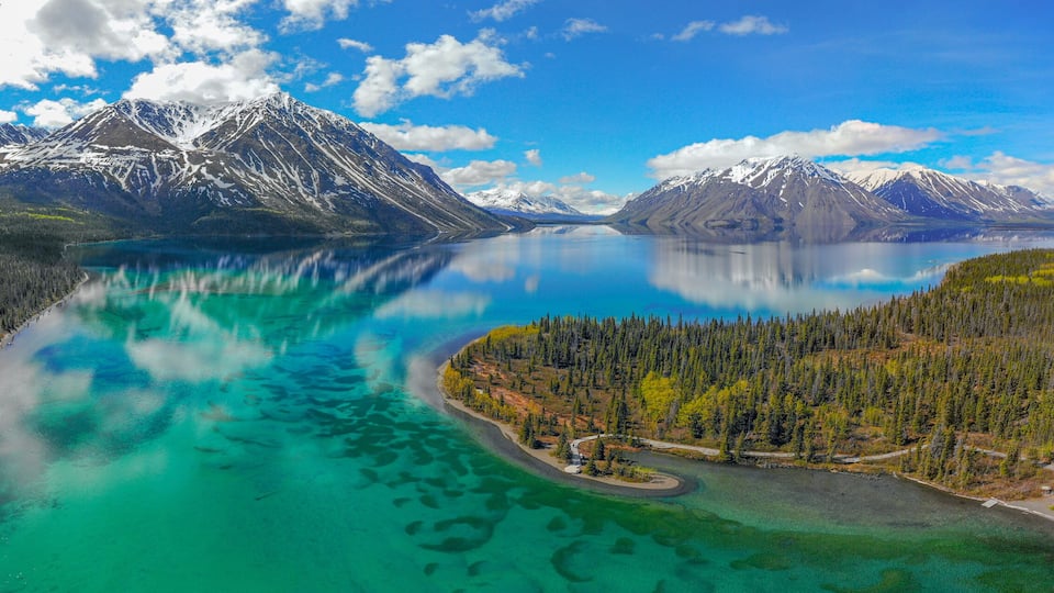 A turquoise lake surrounded by dense forests and snow-capped mountains.
