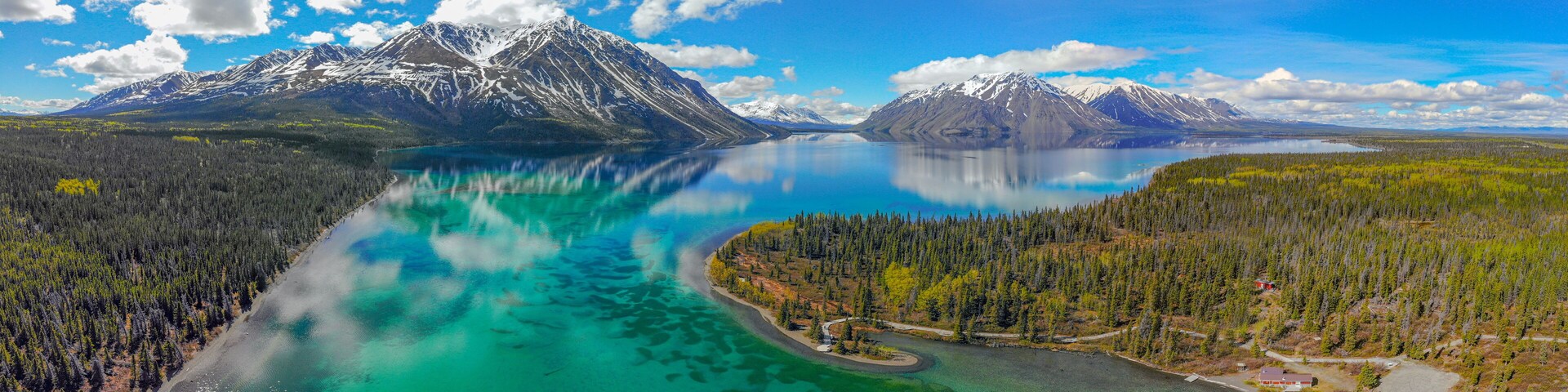 Un lago turquesa rodeado de bosques densos y montañas nevadas.