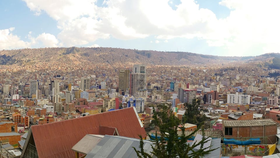 A cityscape with a densely packed urban area, a prominent hill in the background, and a mix of modern and older buildings.