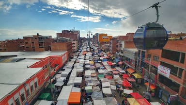 Un mercado callejero concurrido, con numerosos puestos bajo coloridos paraguas, frente a edificios y un teleférico.