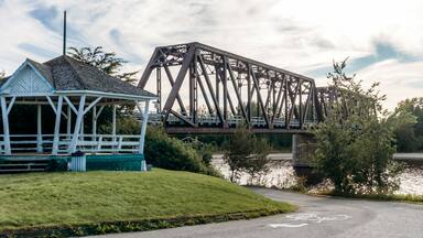 Steel truss bridge crossing a river near the town of Desbiens in Quebec, with riverside park and gazebo in the foreground