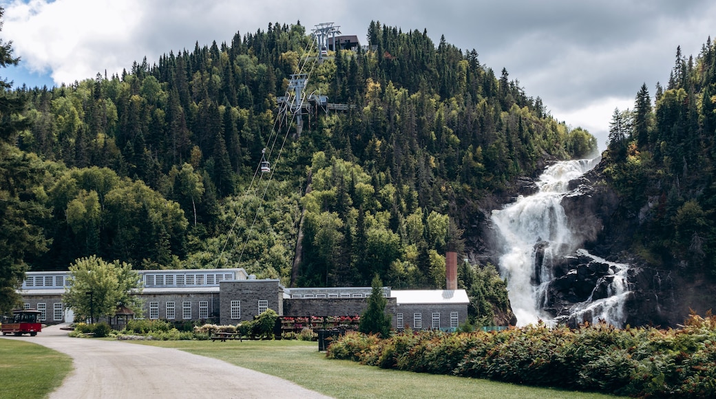 Chambord, Canada - August 18, 2025: Ouiatchouan Falls with old stone mill buildings and aerial tramway at Val-Jalbert Historical Village in Quebe