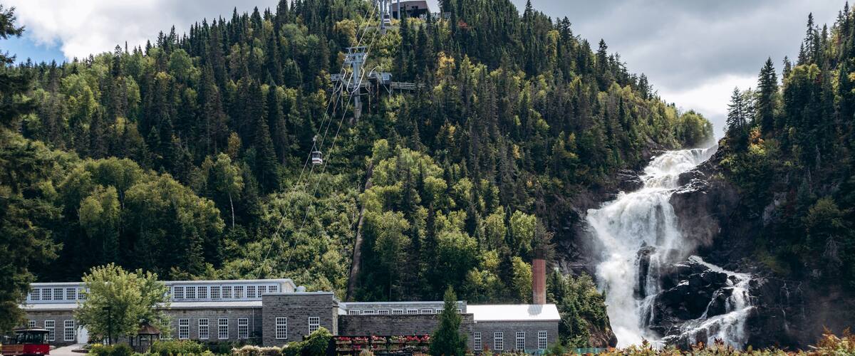 Chambord, Canada - August 18, 2025: Ouiatchouan Falls with old stone mill buildings and aerial tramway at Val-Jalbert Historical Village in Quebe