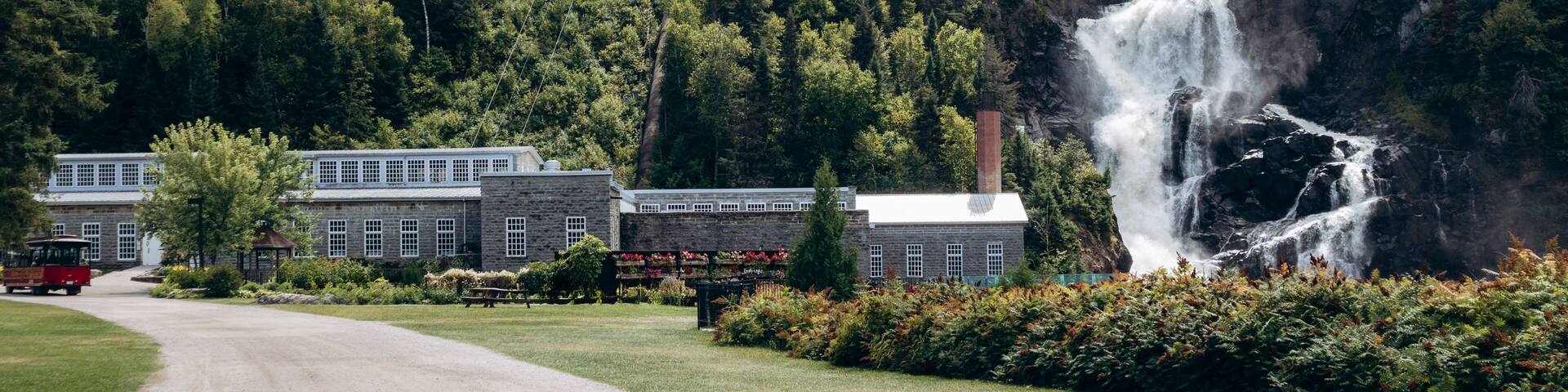 Chambord, Canada - August 18, 2025: Ouiatchouan Falls with old stone mill buildings and aerial tramway at Val-Jalbert Historical Village in Quebe