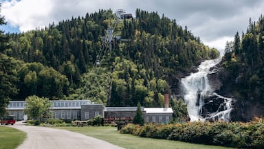 Chambord, Canada - August 18, 2025: Ouiatchouan Falls with old stone mill buildings and aerial tramway at Val-Jalbert Historical Village in Quebe