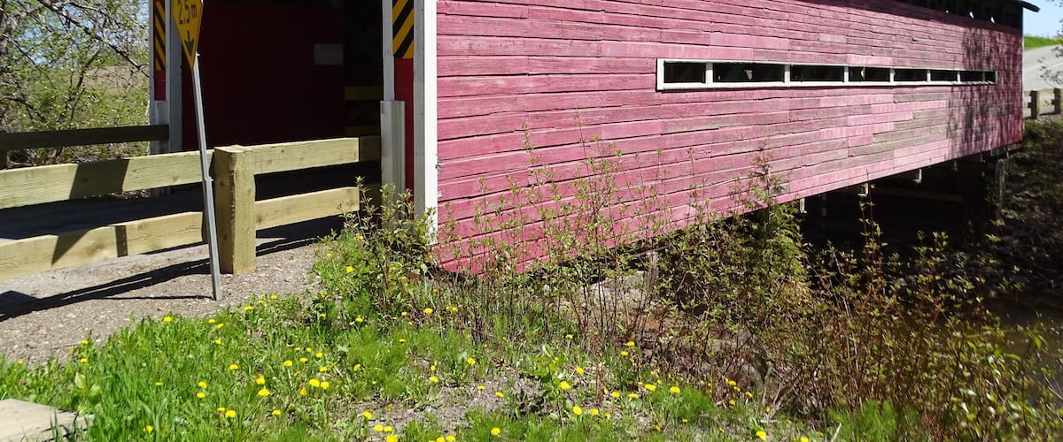 A red covered bridge with a wooden entrance and a metal roof.