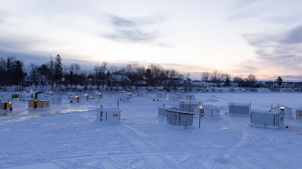 A snowy landscape with several small buildings and a few trees.