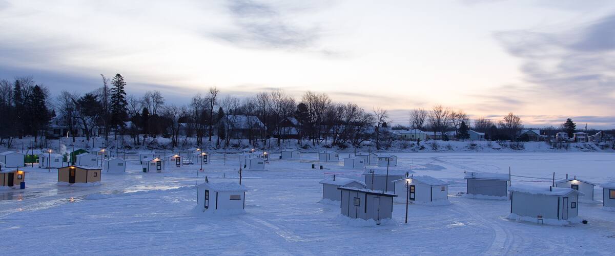 A snowy landscape with several small buildings and a few trees.