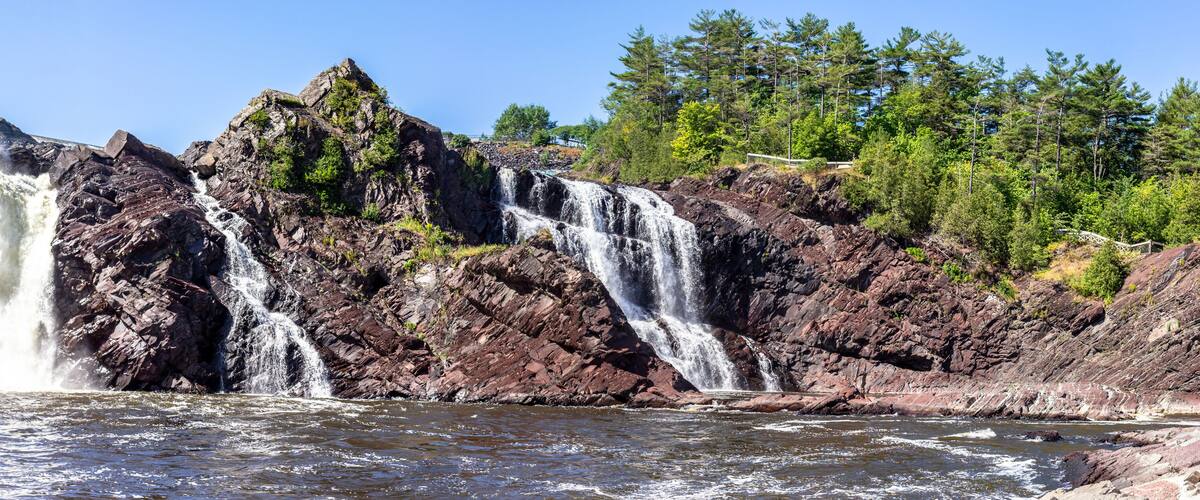 A multi-tiered waterfall cascading over rocky terrain with dense forest in the background.