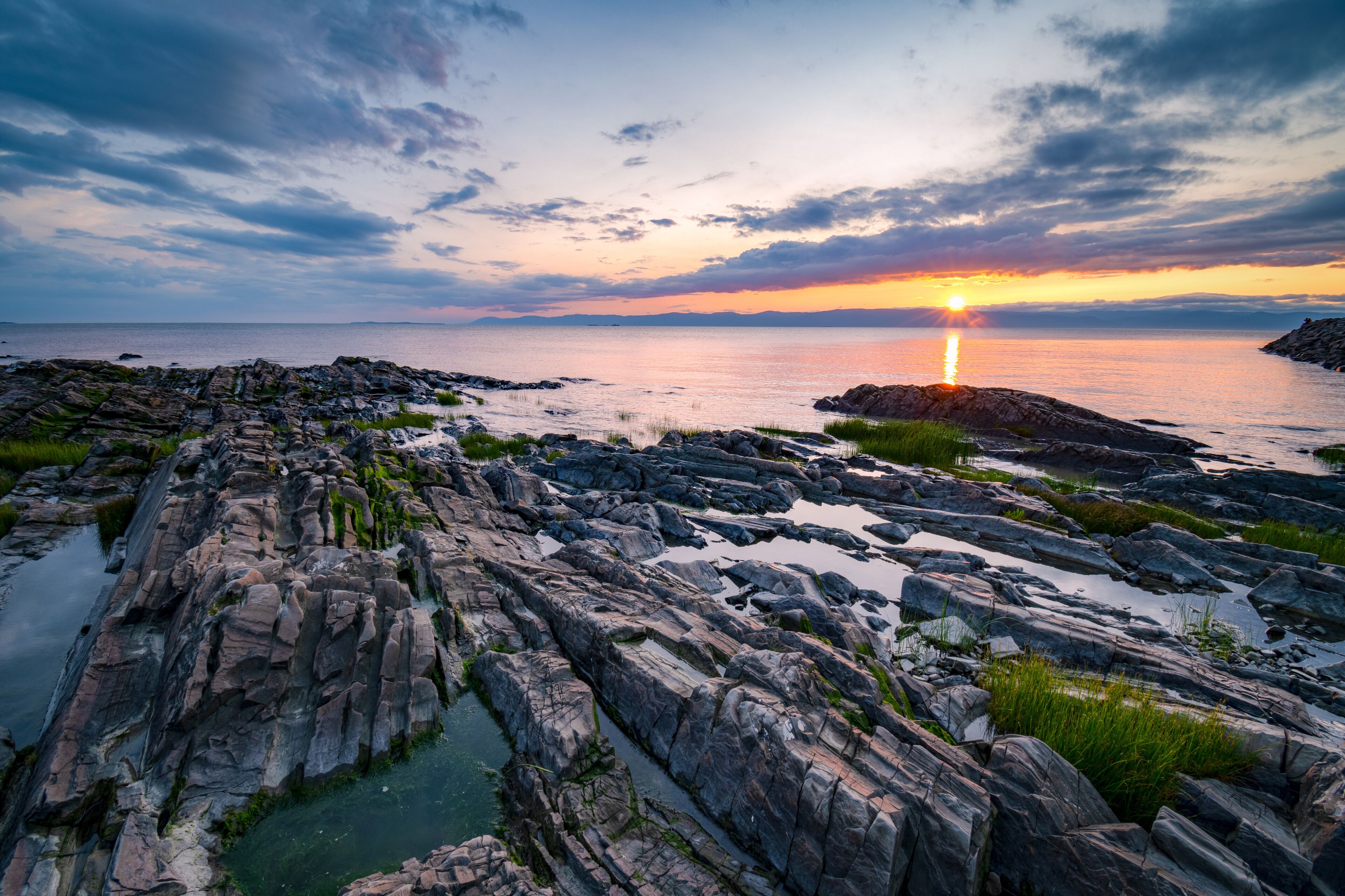 A rocky shoreline with a sunset over the ocean.