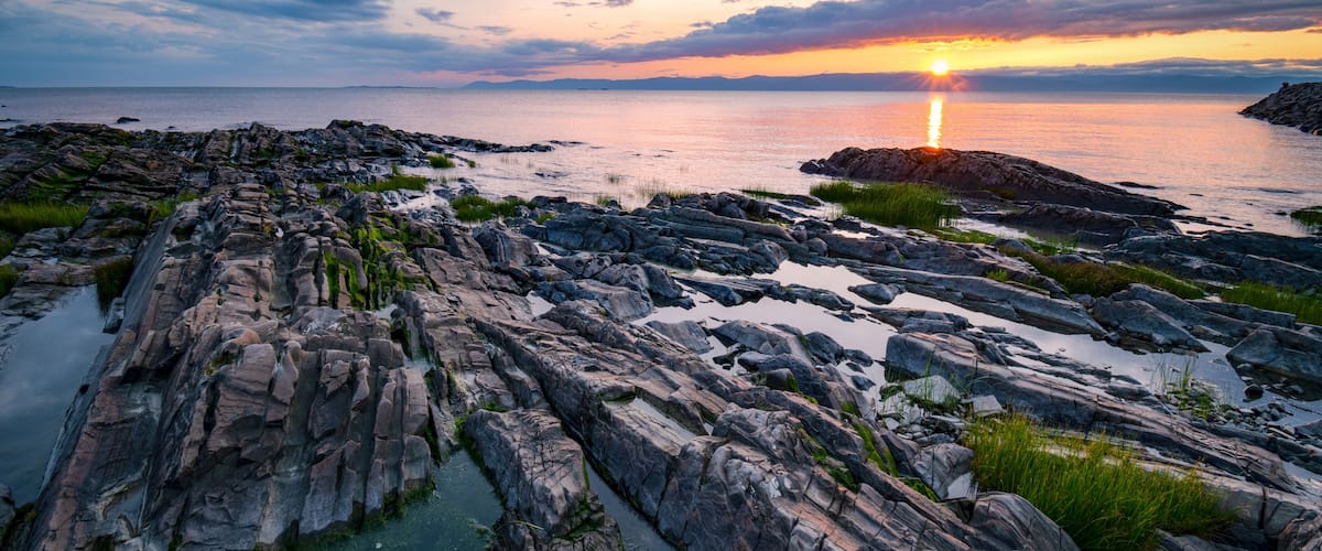 A rocky shoreline with a sunset over the ocean.