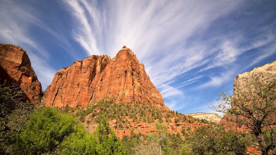 A red rock canyon with a prominent peak and lush greenery at its base.