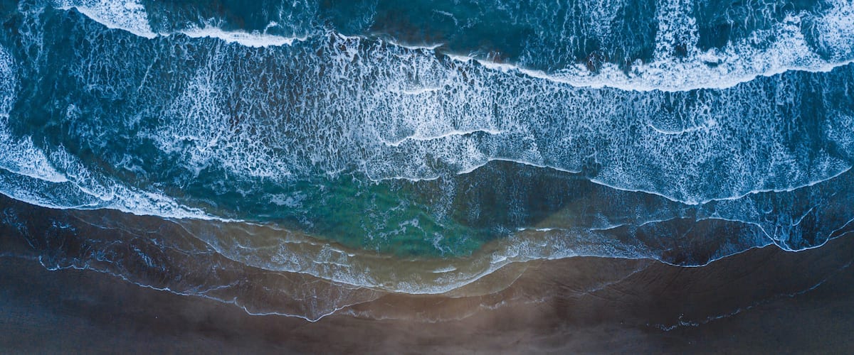An aerial view of a beach with waves crashing onto the shore and a small boat near the water's edge.