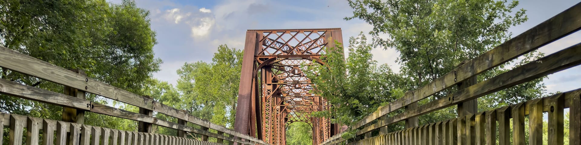 A wooden bridge with metal trusses, surrounded by trees.
